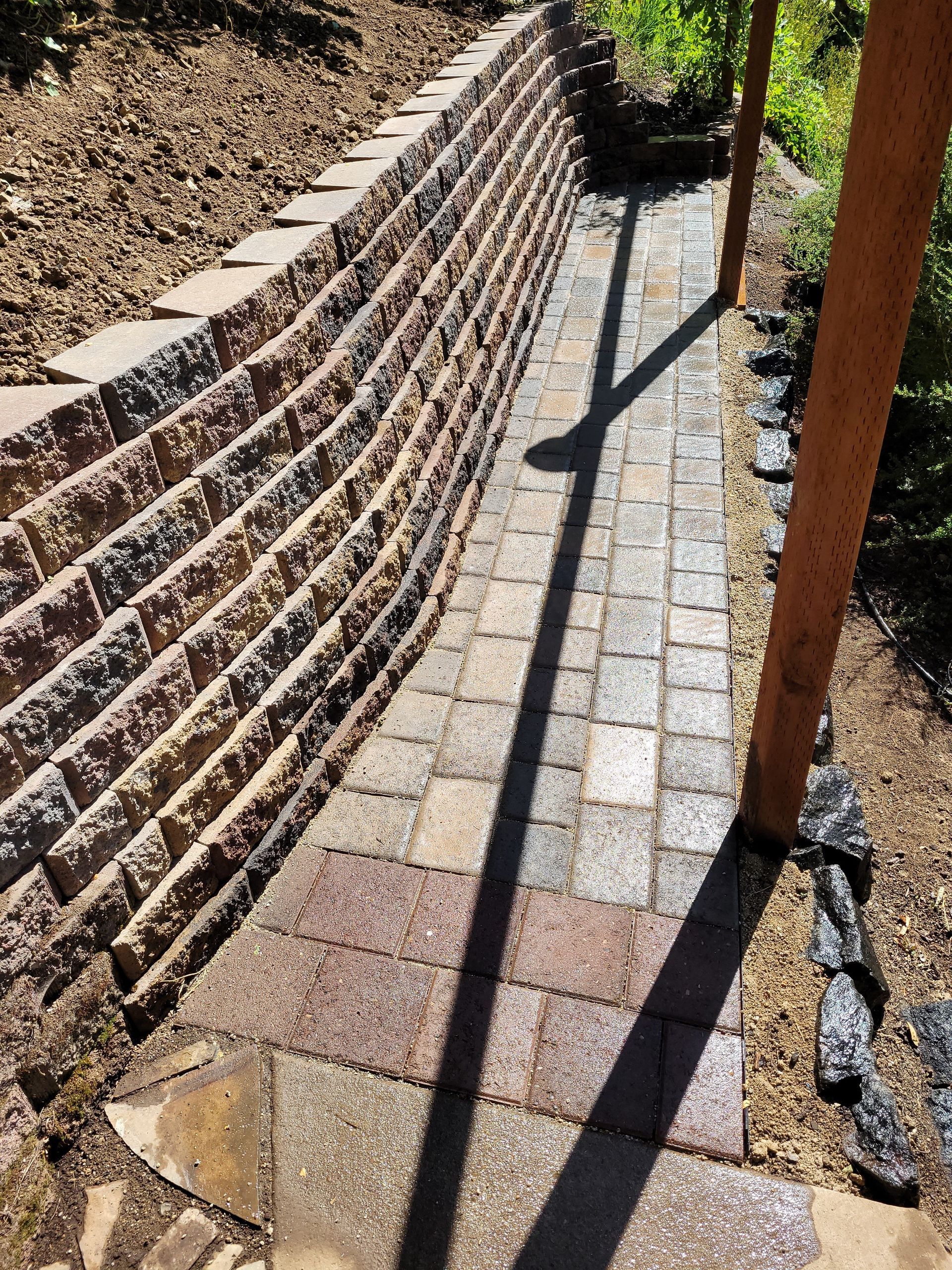 Curved brick walkway beside a retaining wall, with gravel edges and long shadows in sunlight