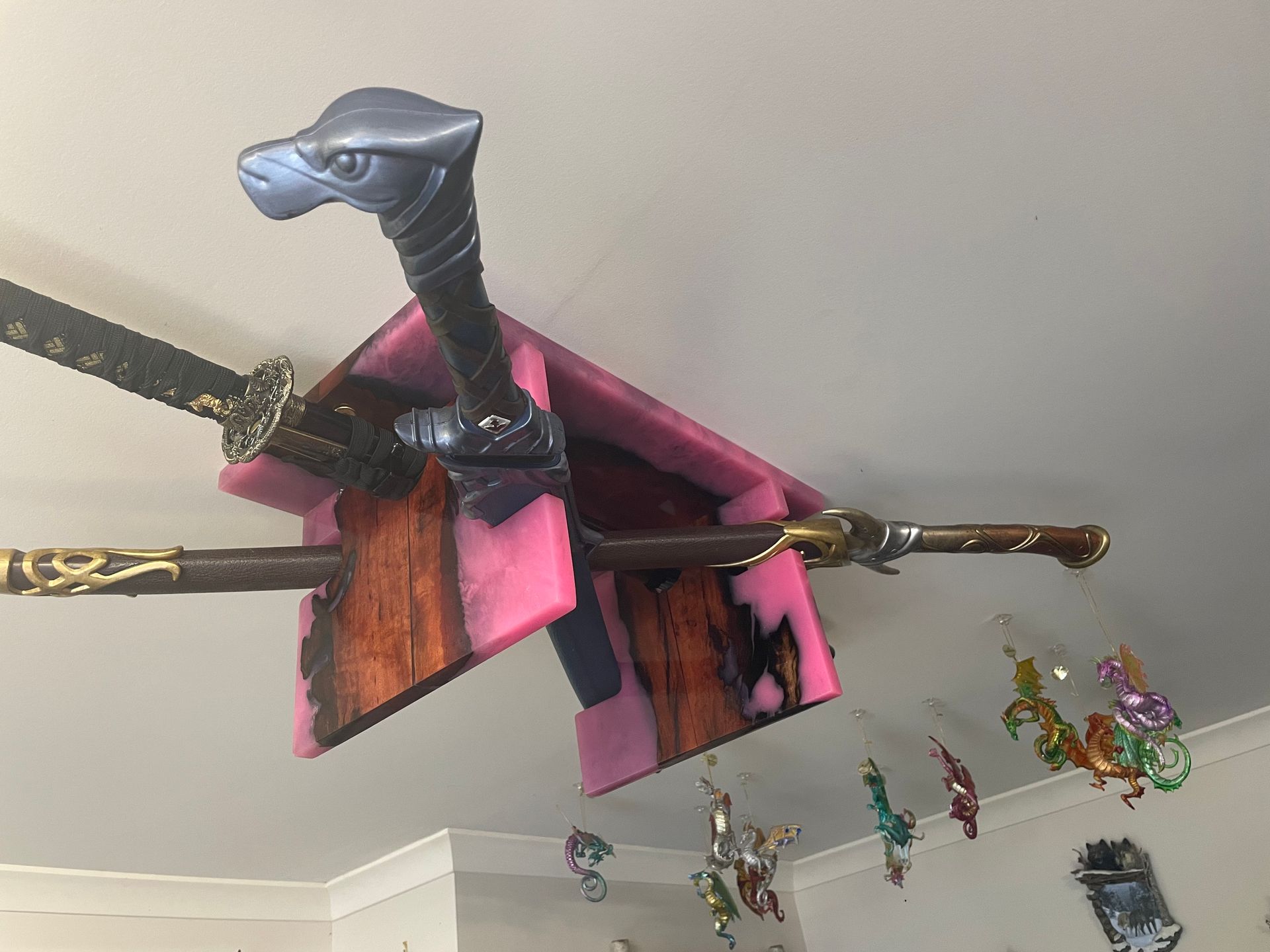 Swords displayed on a pink and wood-toned ceiling-mounted rack, small toy figures hanging below.