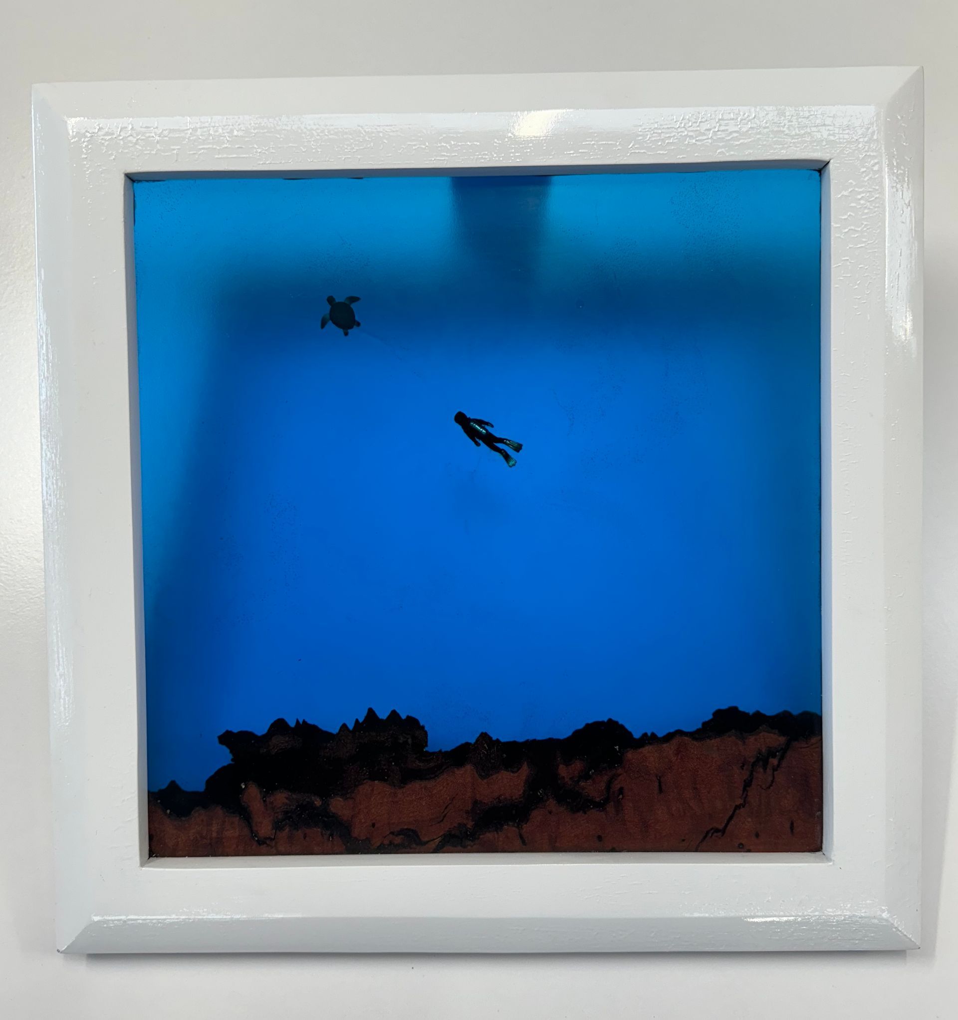 A diver and sea turtle swim above a coral reef in a blue ocean, encased in a white-framed box.