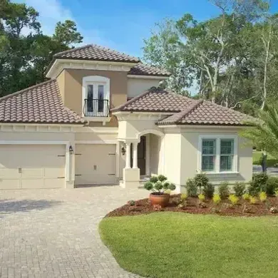 A white house with a brown tile roof and a brick driveway