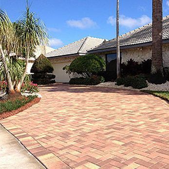 A brick driveway leading to a house with palm trees.