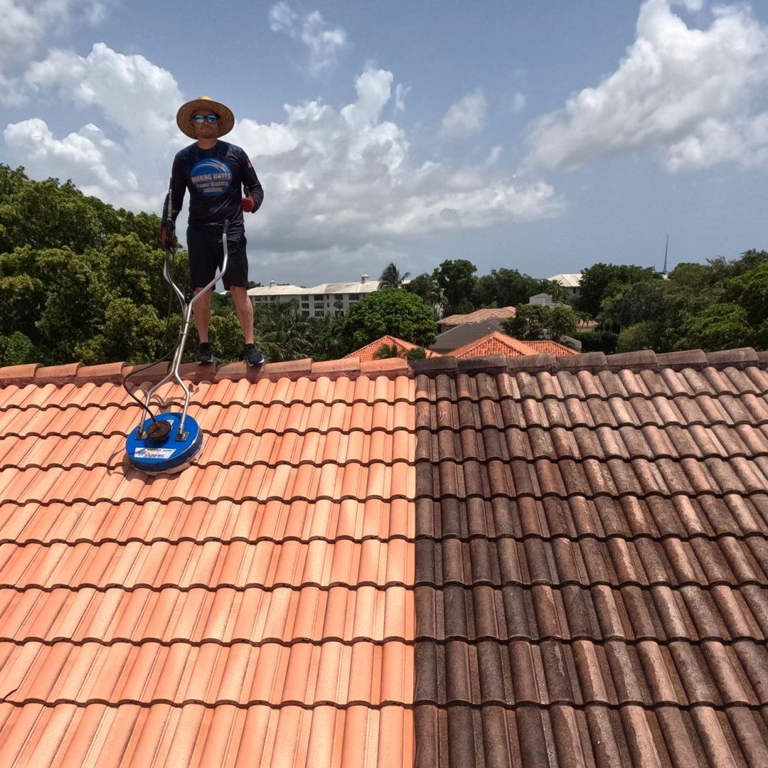 A man is standing on top of a tiled roof cleaning it