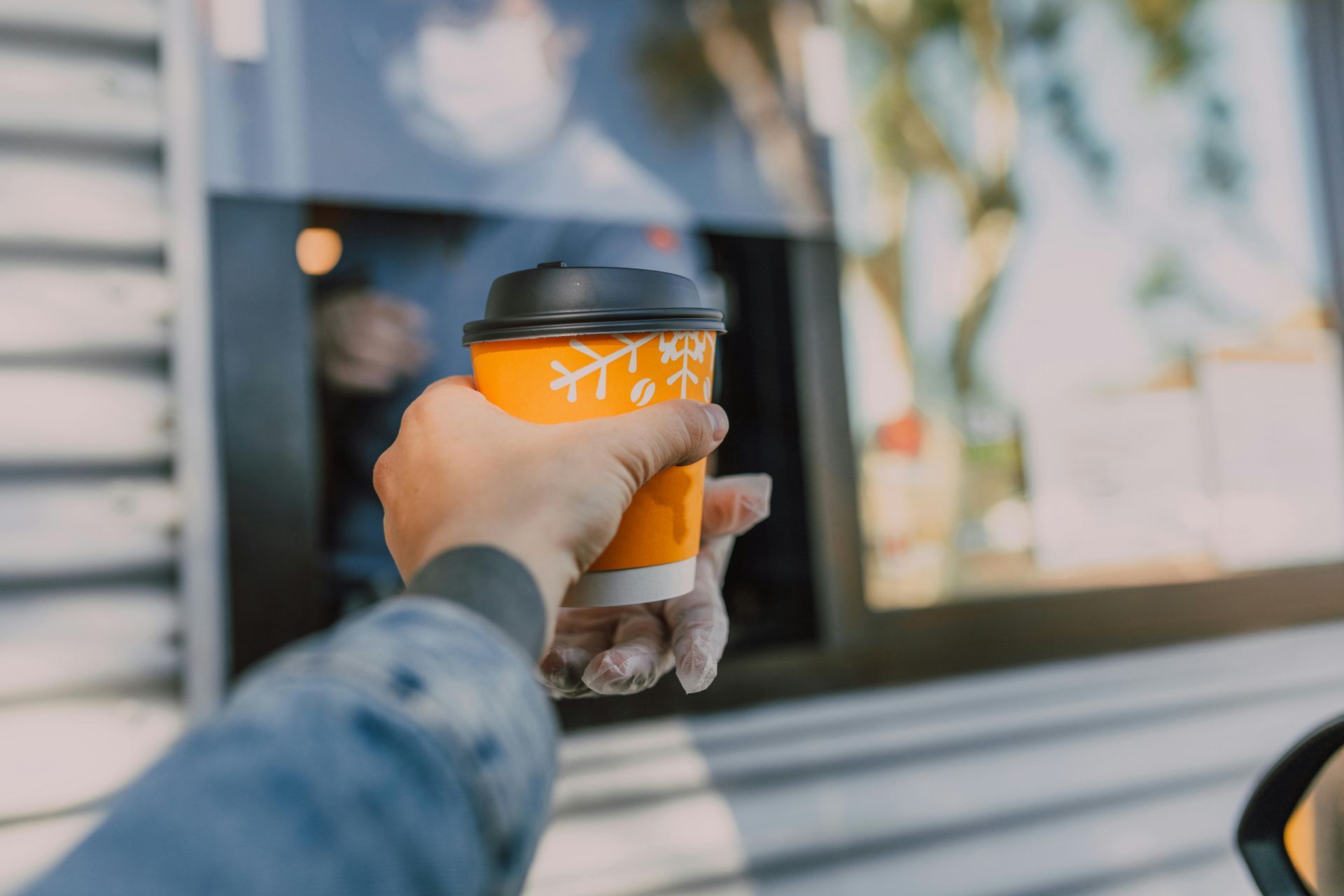 A person is holding a cup of coffee in front of a drive through window.