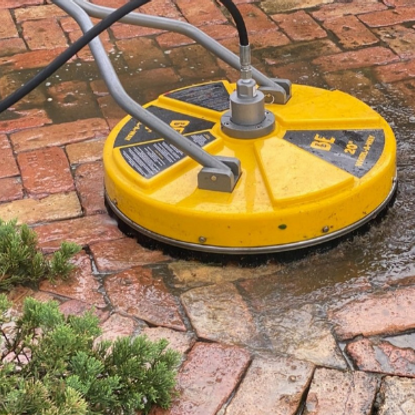 A yellow machine is cleaning a brick walkway