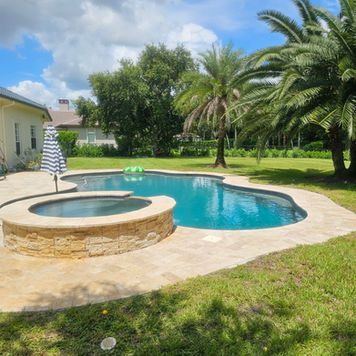 A large swimming pool with a hot tub in the backyard surrounded by palm trees.