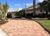 A brick driveway leading to a house with a palm tree in the background.