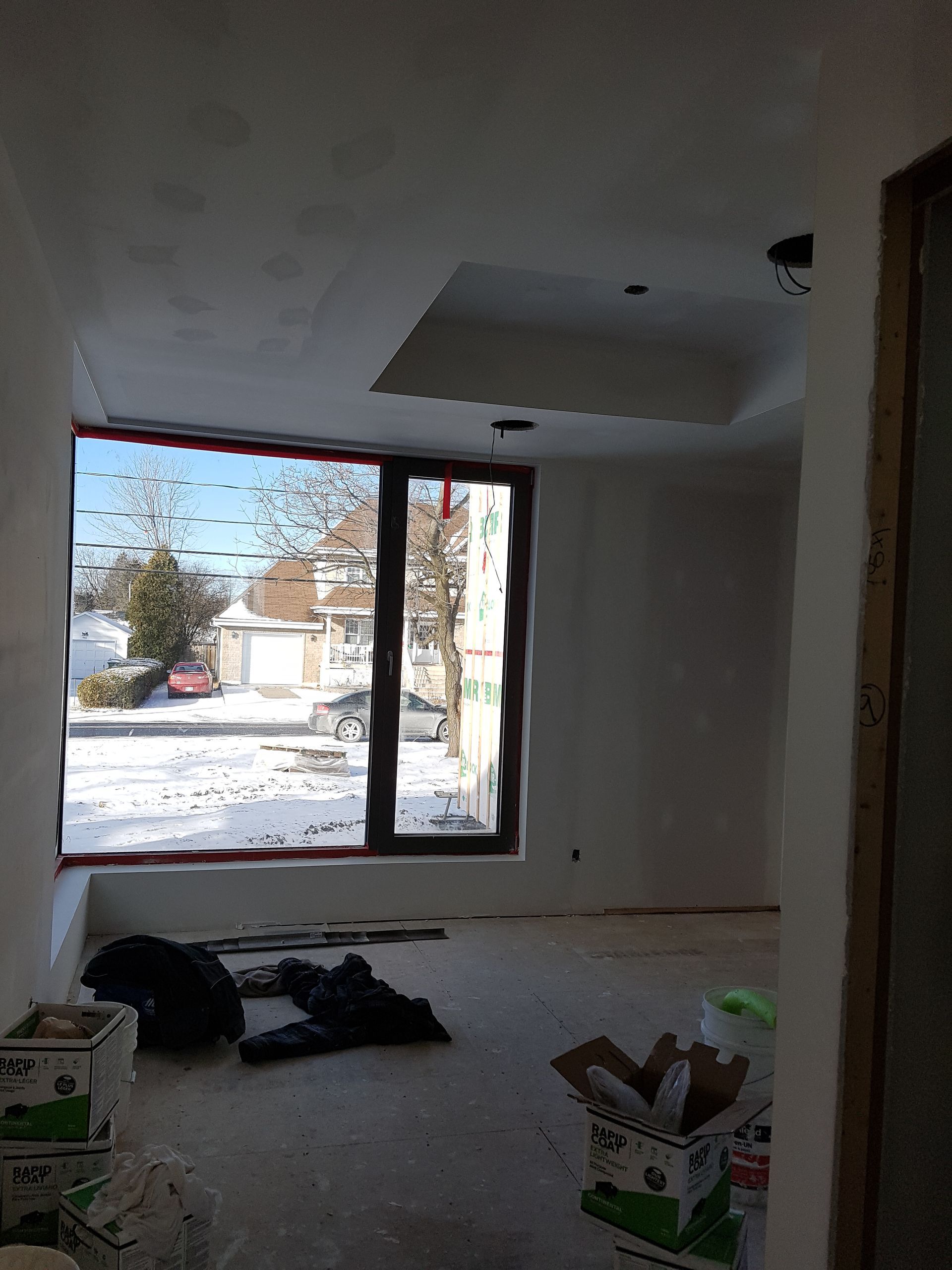 Une pièce avec une grande fenêtre et des caisses au sol.