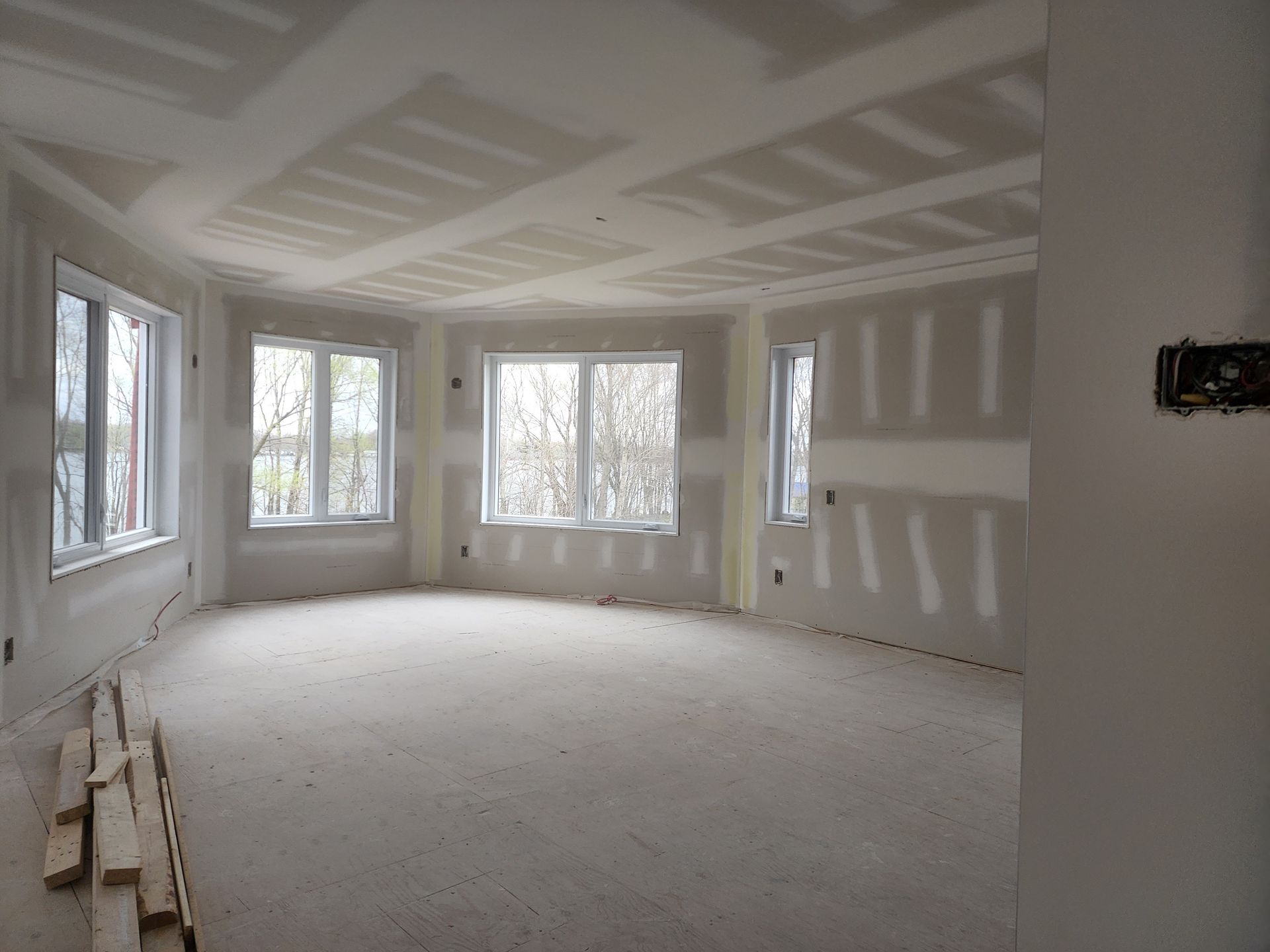 Une pièce vide avec beaucoup de fenêtres et des cloisons sèches sur les murs.