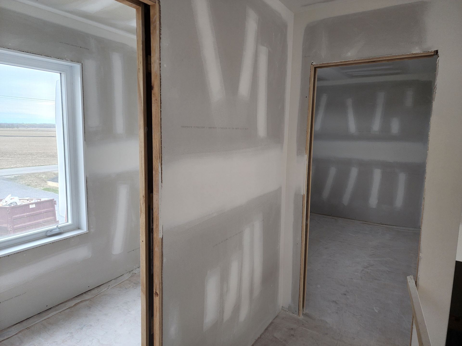 Un couloir avec des murs en plaques de plâtre et une fenêtre dans une maison en construction.