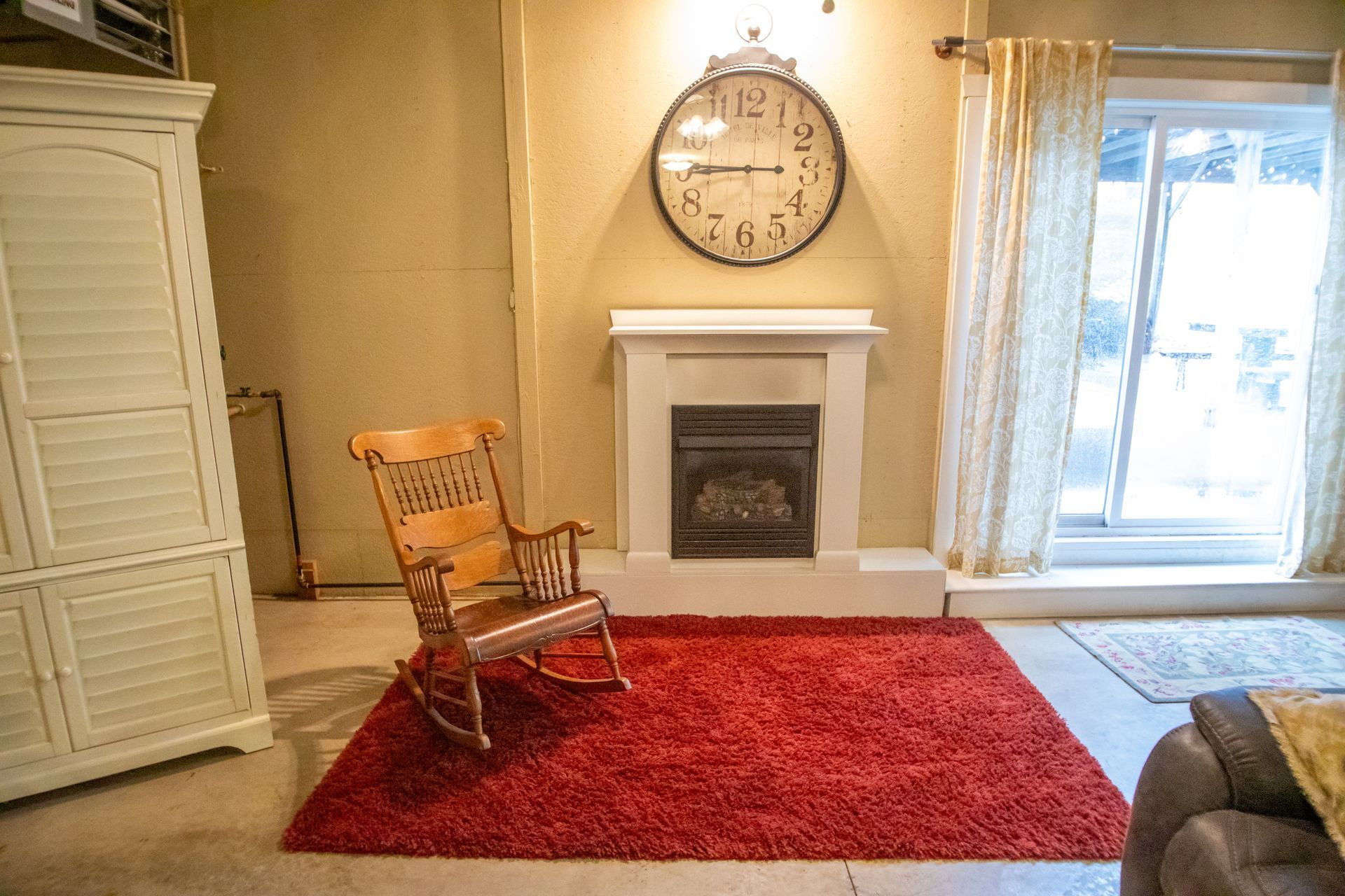 Living room with red rug, rocking chair, fireplace, and large clock.