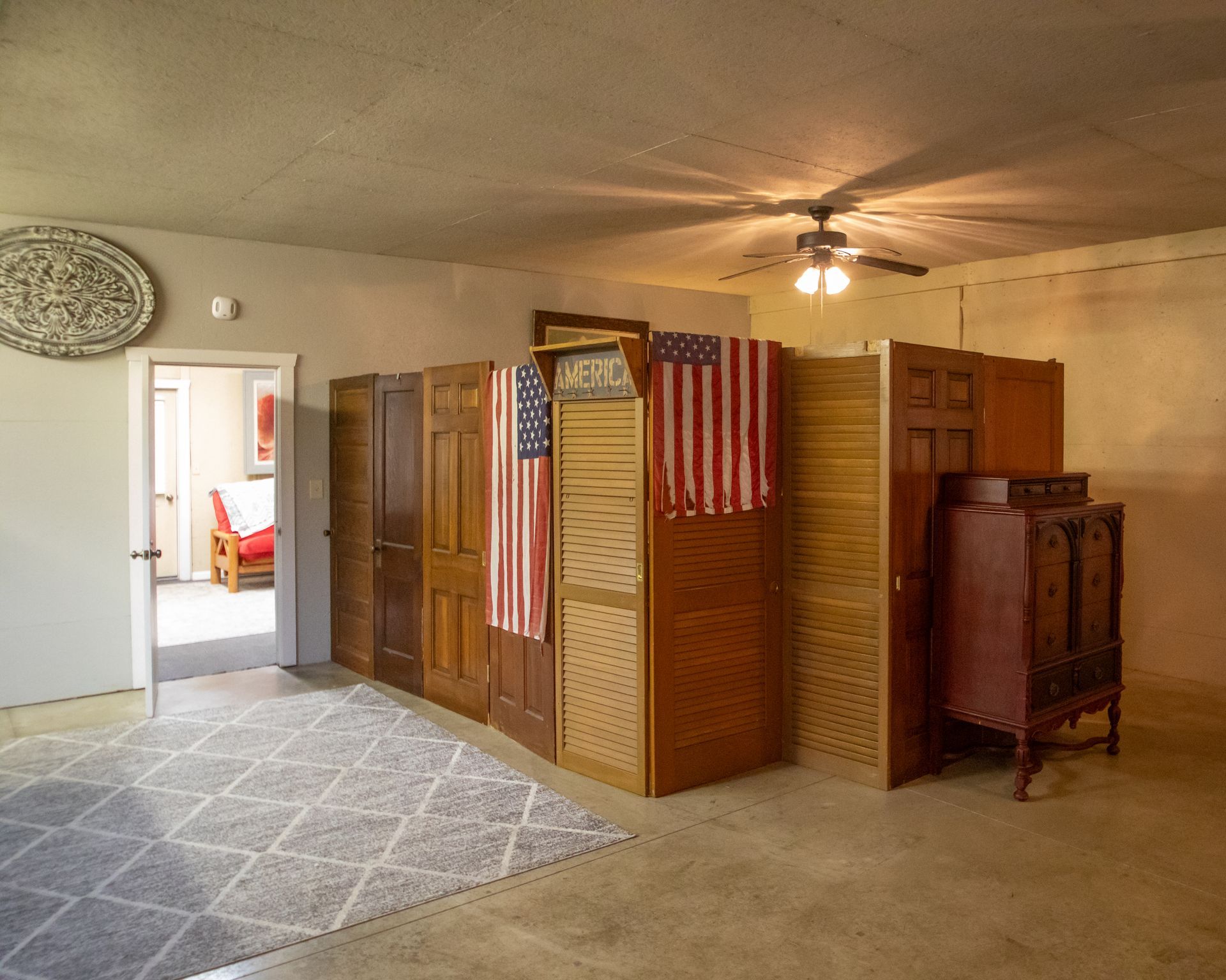 Room with a partition made of repurposed doors and American flags. A rug and ceiling fan are visible.