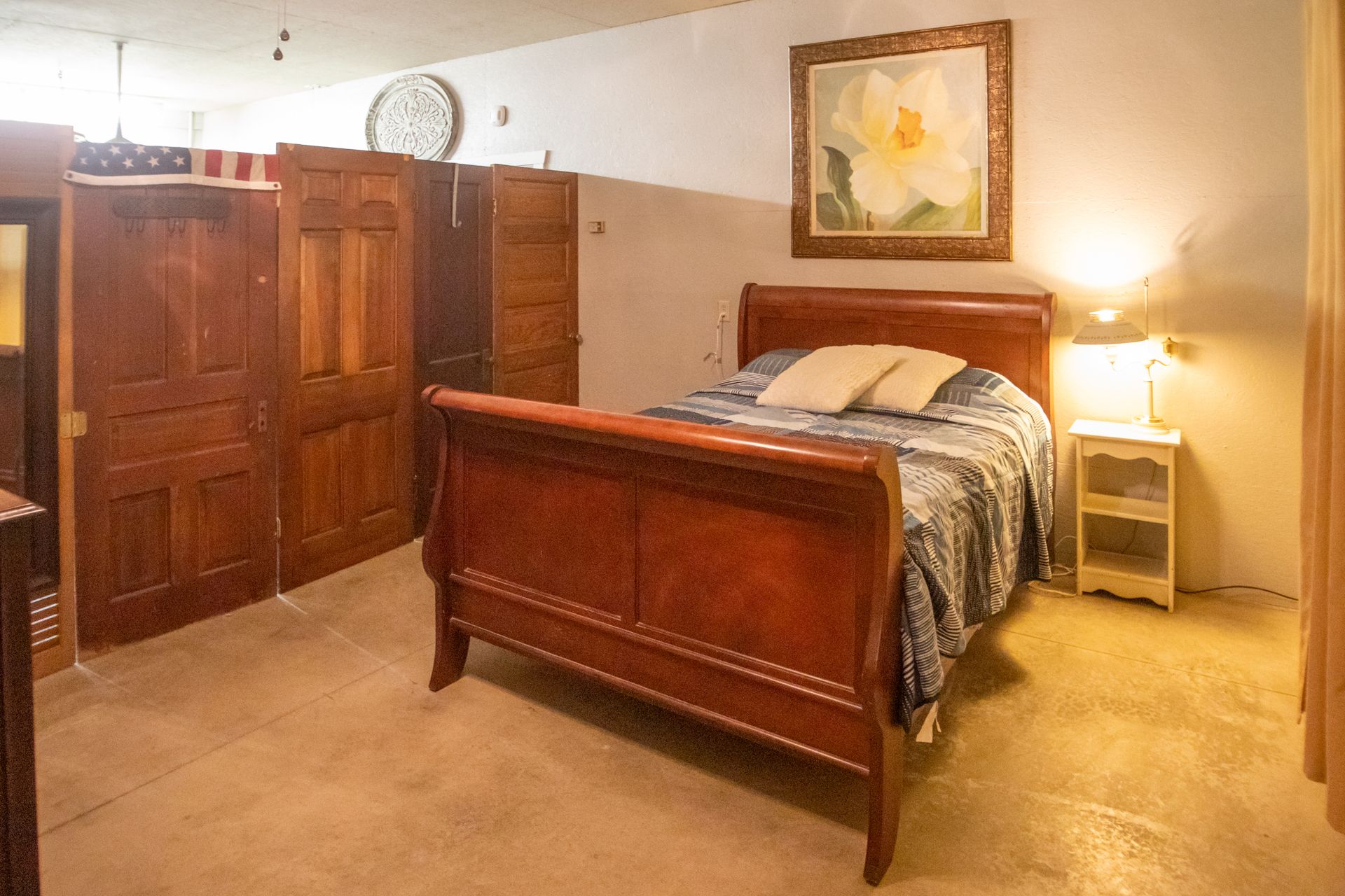 Bedroom with antique bed, nightstand, and framed floral art; doors form a partial wall.