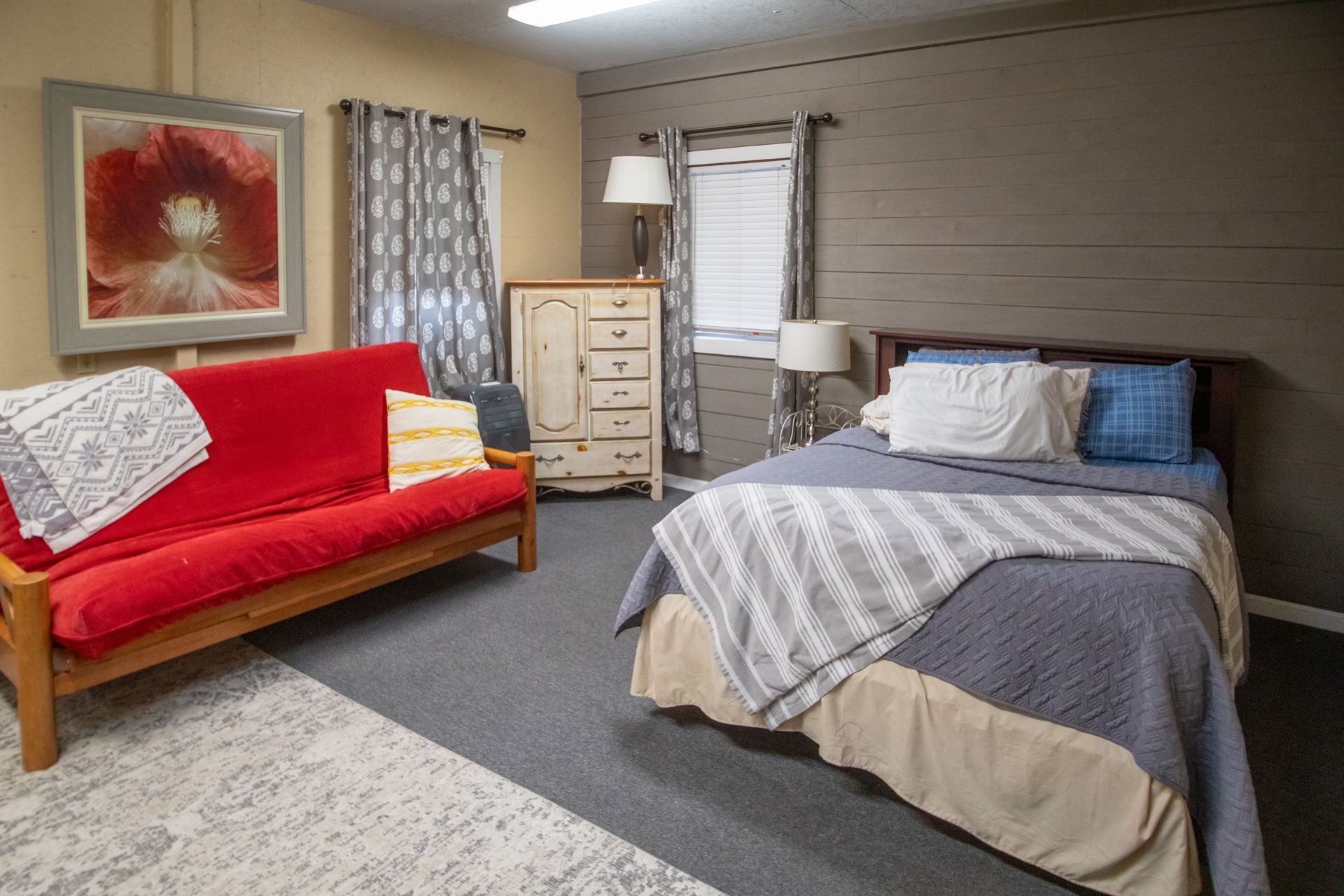 Bedroom with red futon, double bed, gray walls, dresser, and poppy artwork.