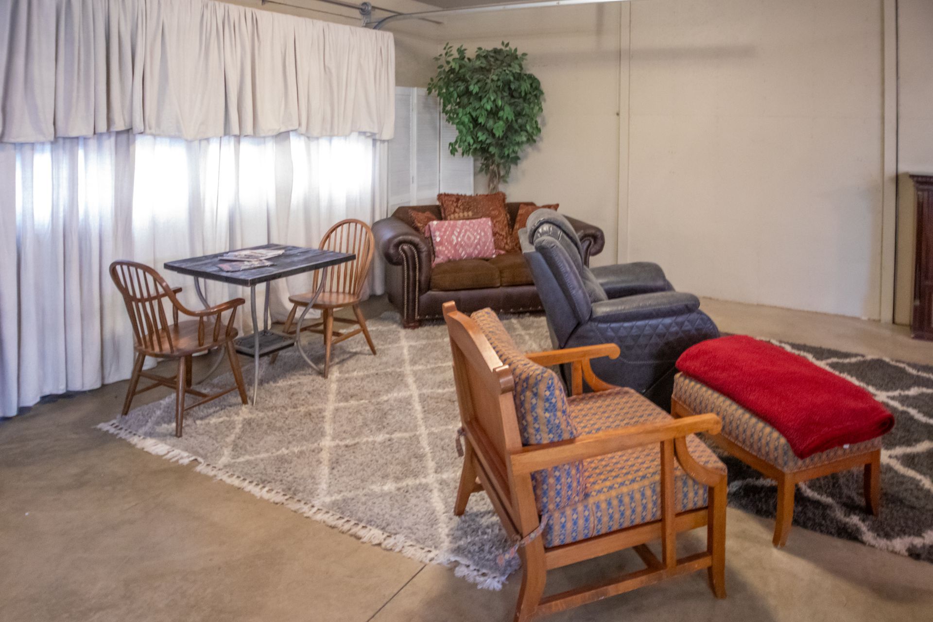 Living room setting with furniture on a rug; includes a sofa, chairs, table, and curtains.