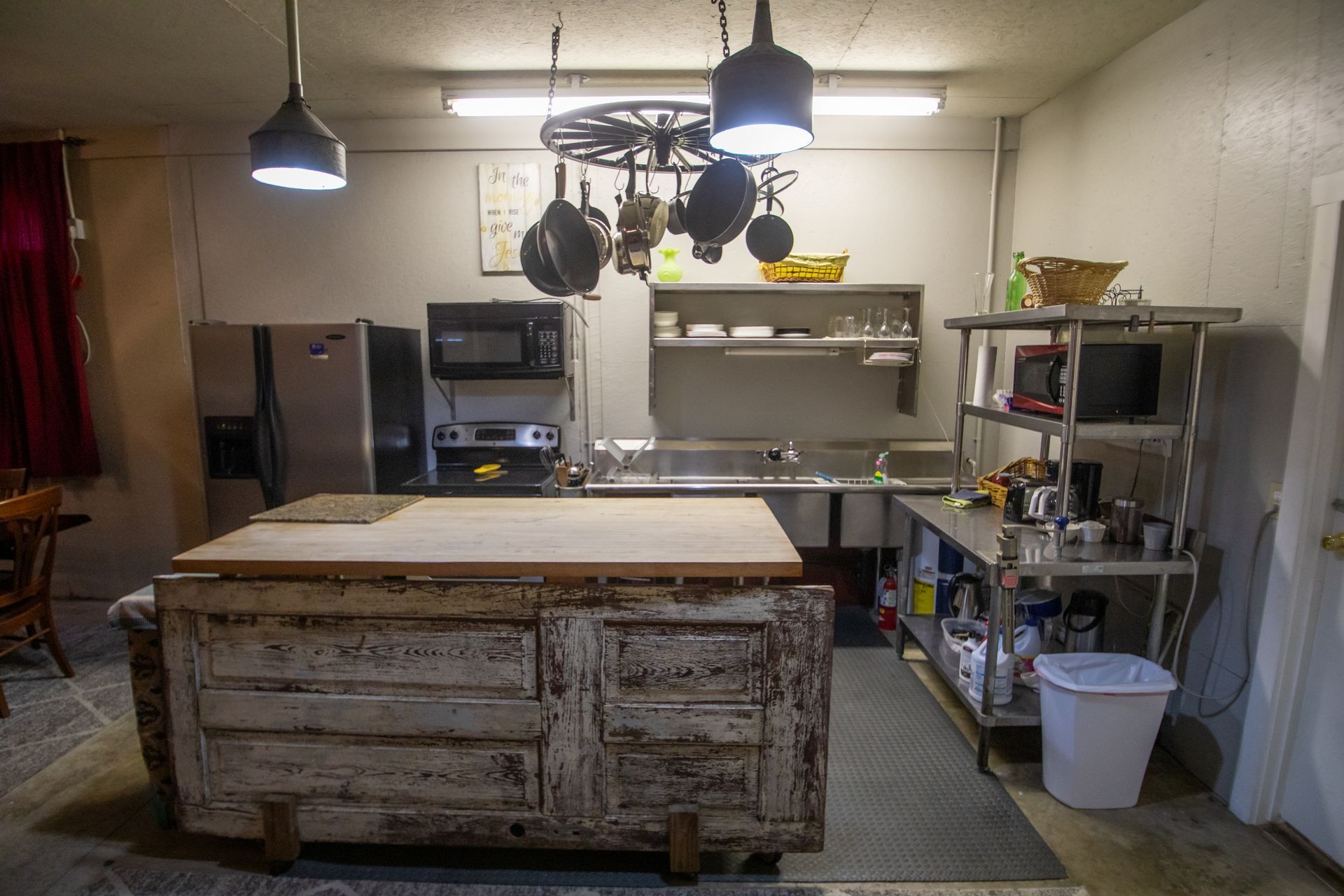 Rustic kitchen with a large island, stainless steel counters, and hanging pots.
