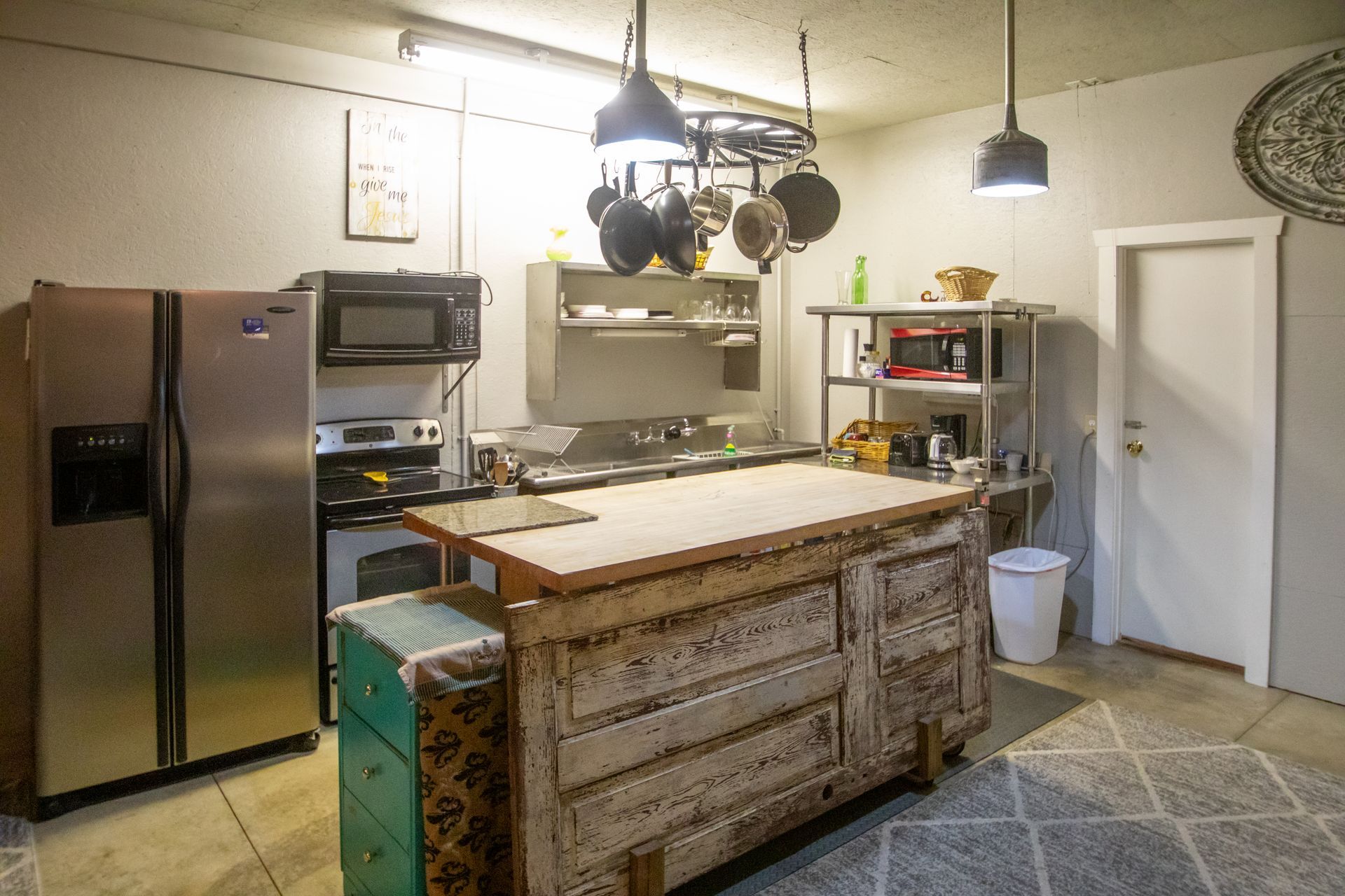 Kitchen with island and stainless steel appliances. Pots hang above island.