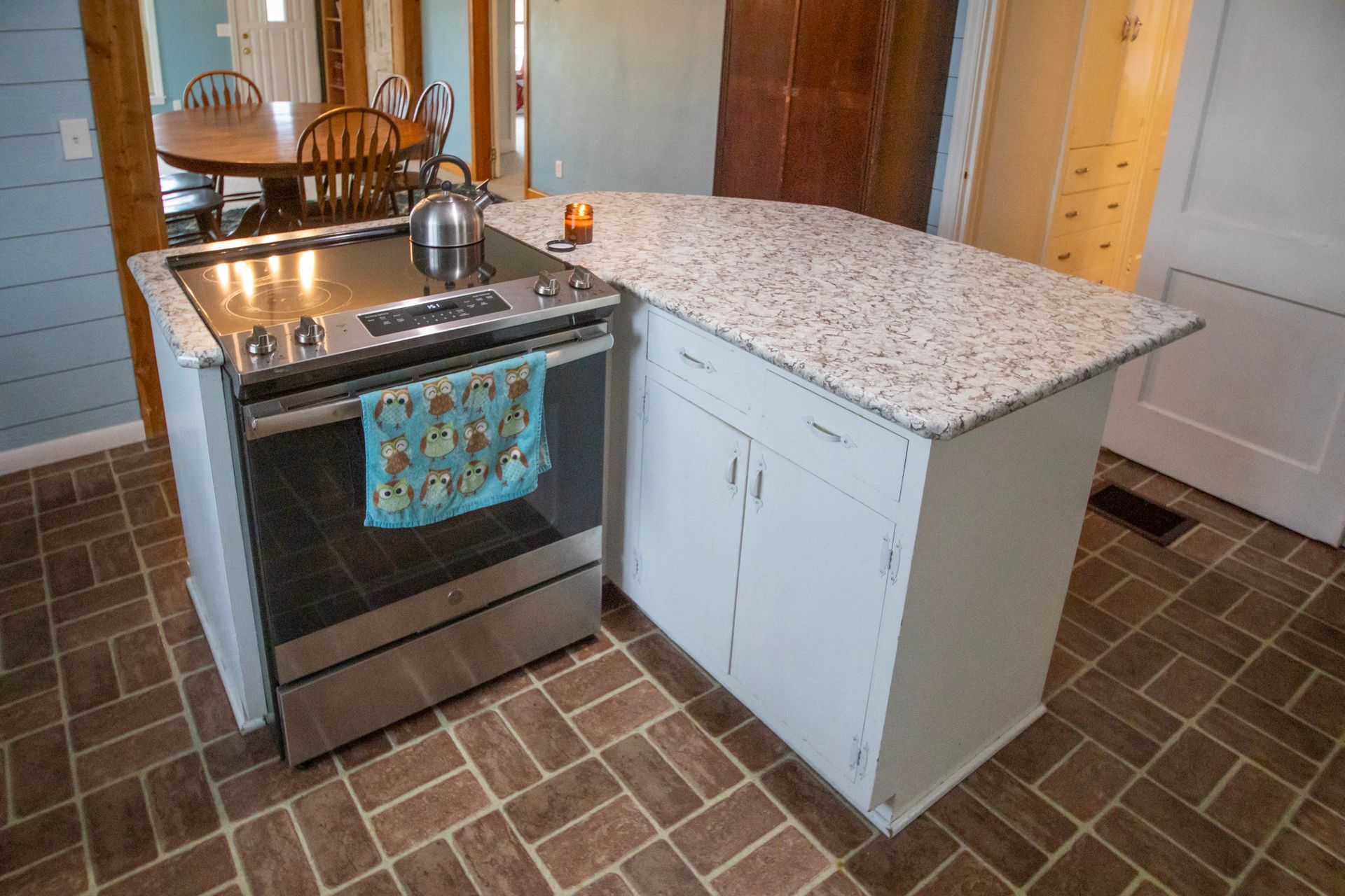 Kitchen island with stove, cabinets, and granite countertop, brick floor.