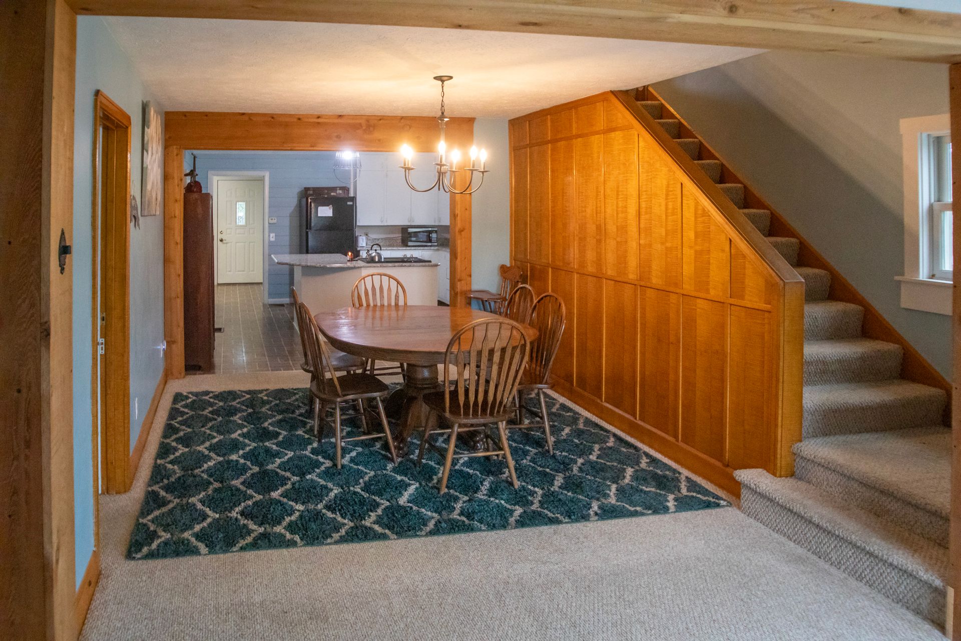 Dining room with a table and chairs on a blue patterned rug, next to a wooden staircase.