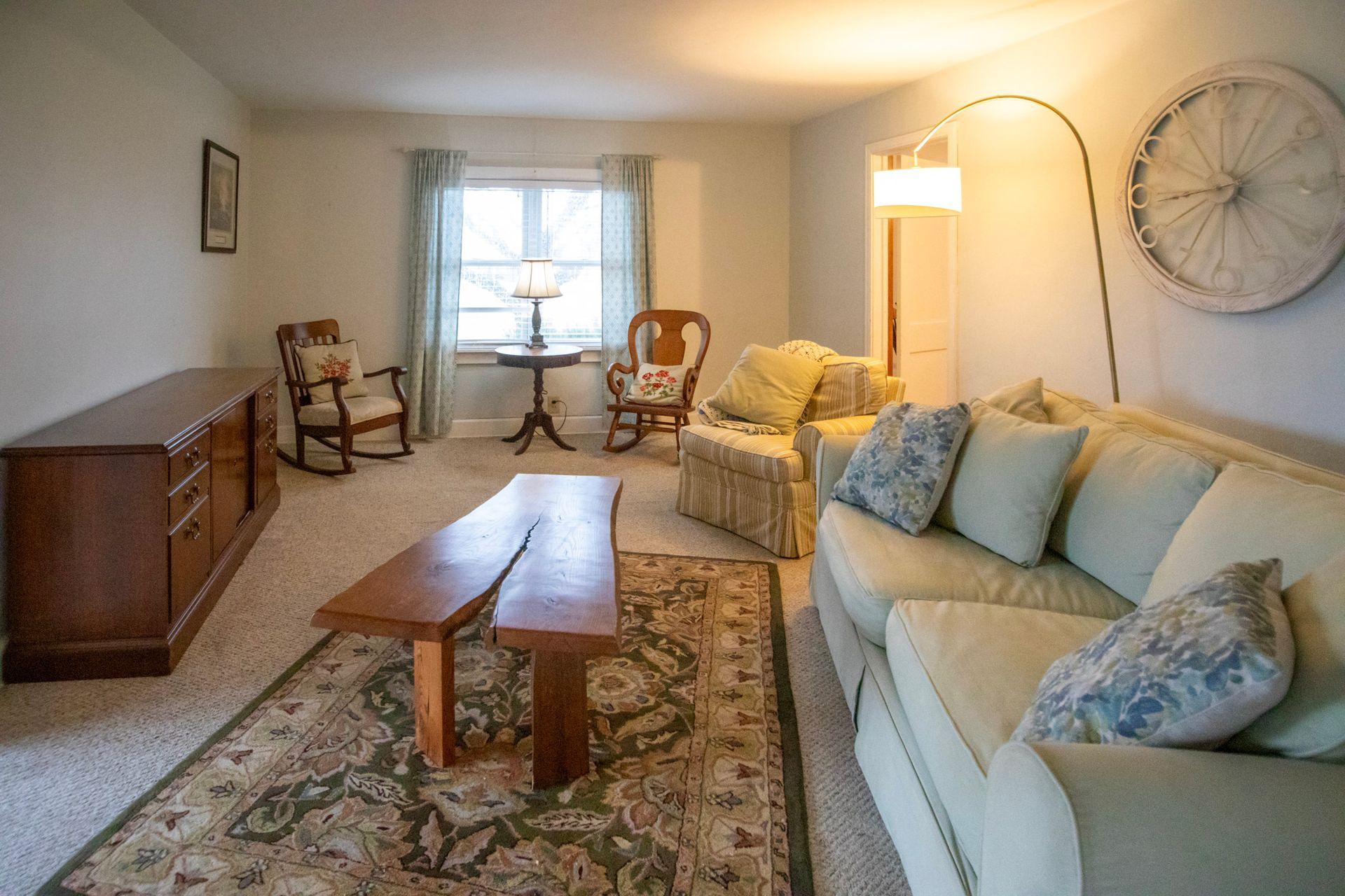 Living room with sofa, coffee table, rug, chairs, wooden cabinet, and decorative wheel.