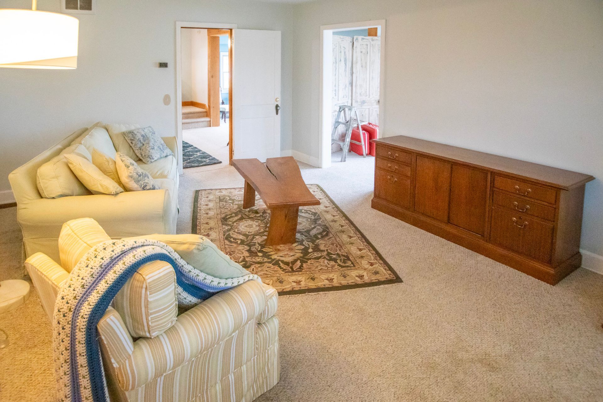 Living room with beige furniture, wooden bench, rug, and cabinet. Open doorways reveal additional rooms.