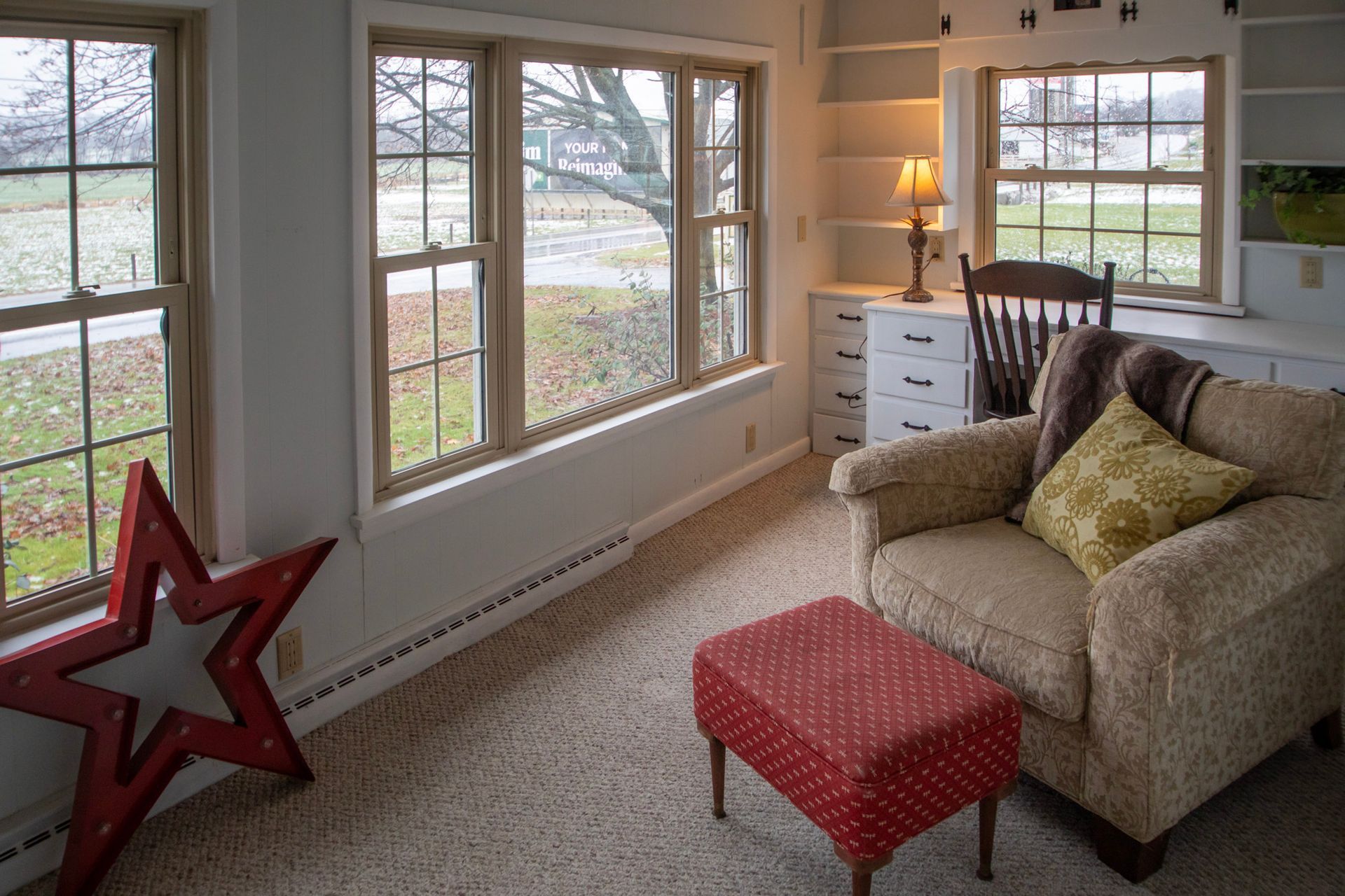 Cozy sunroom with a chair, ottoman, and star decor near windows overlooking a grassy yard.