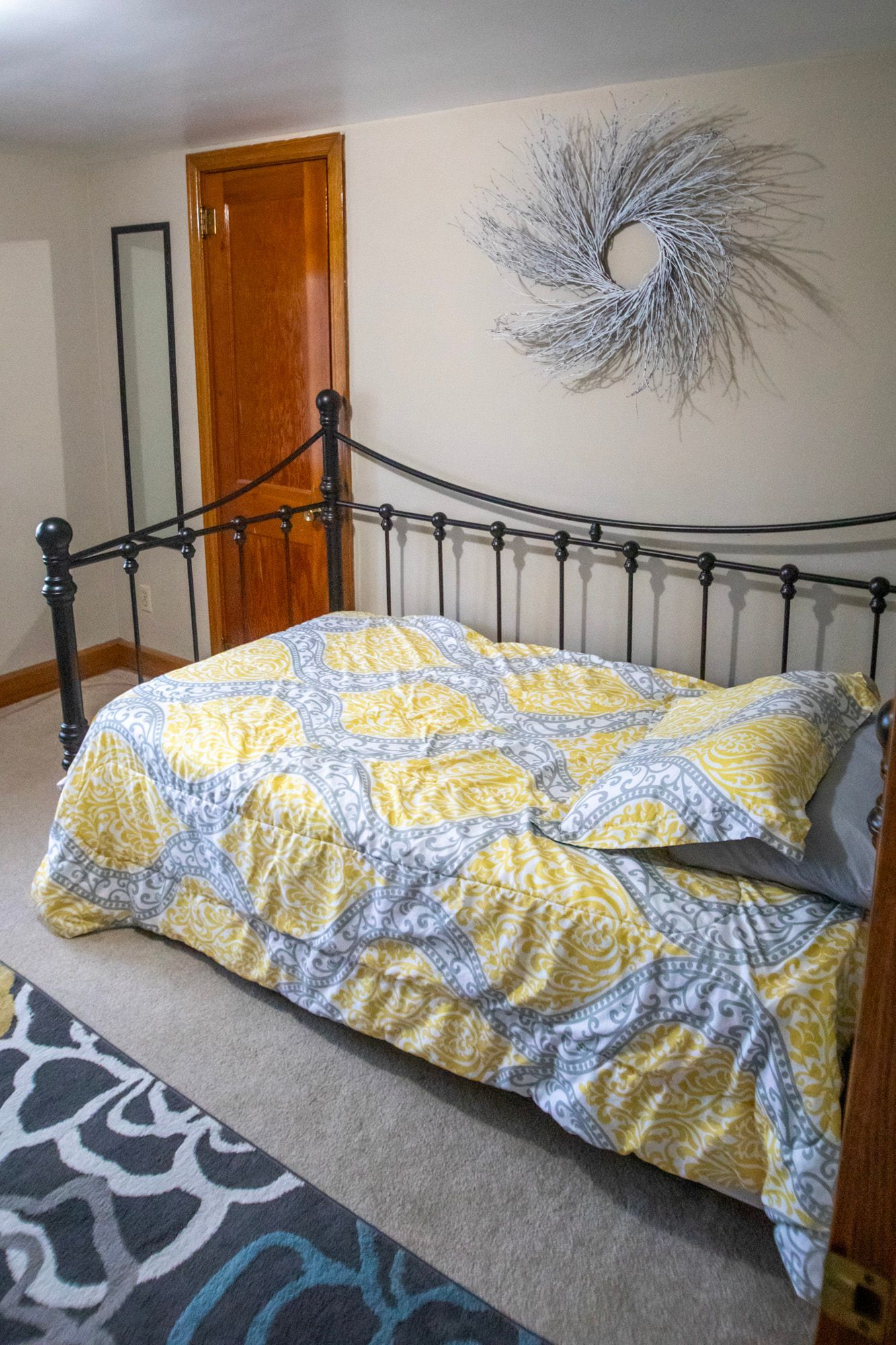 Bedroom with wrought iron bed, yellow patterned quilt, and artwork on the wall.