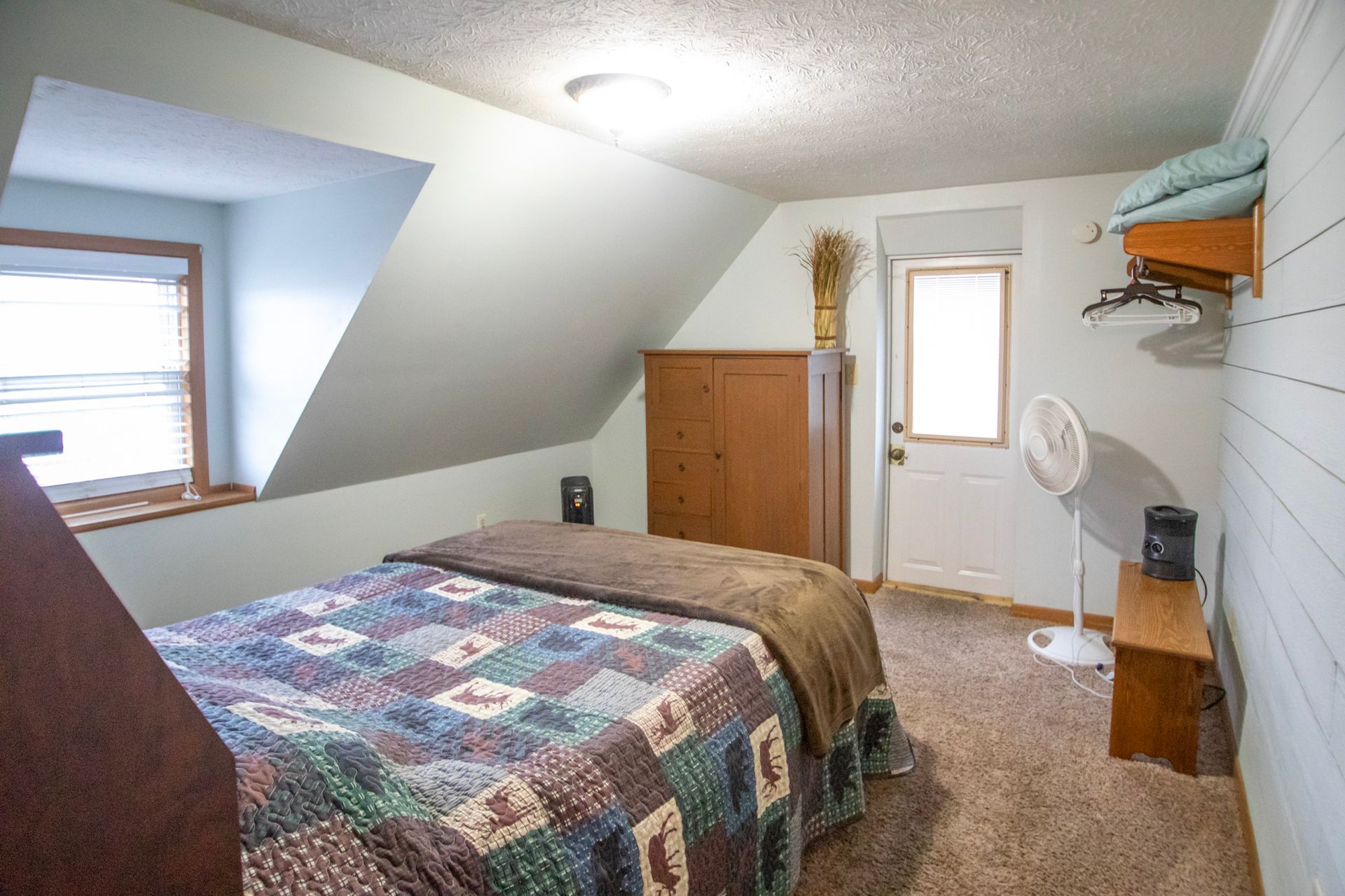 Bedroom with angled ceiling, bed, wooden cabinet, and door to outside.