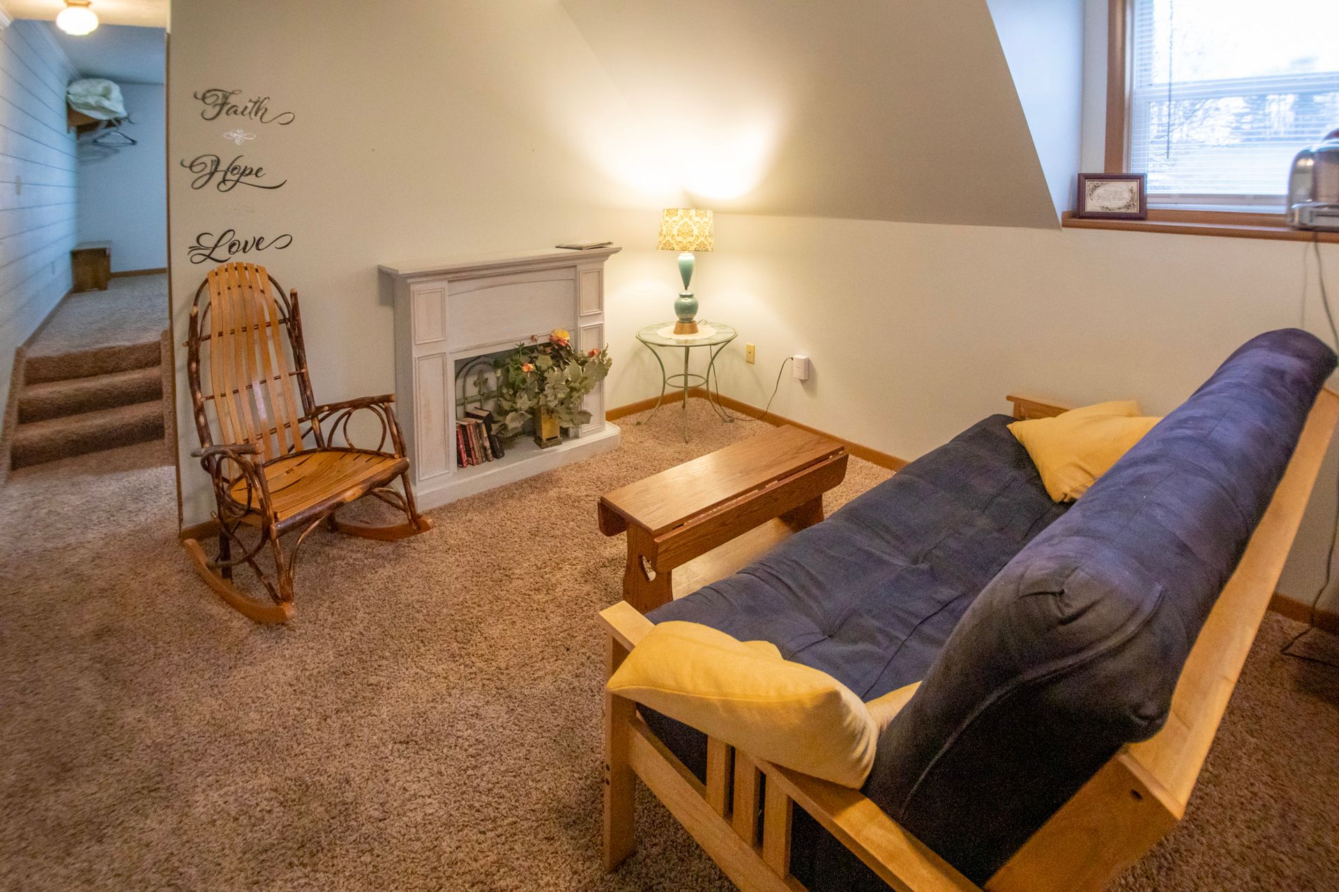 Cozy living area with futon, rocking chair, faux fireplace, and wall text 