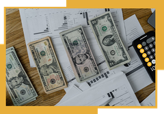 Three stacks of money are sitting on top of a wooden table.