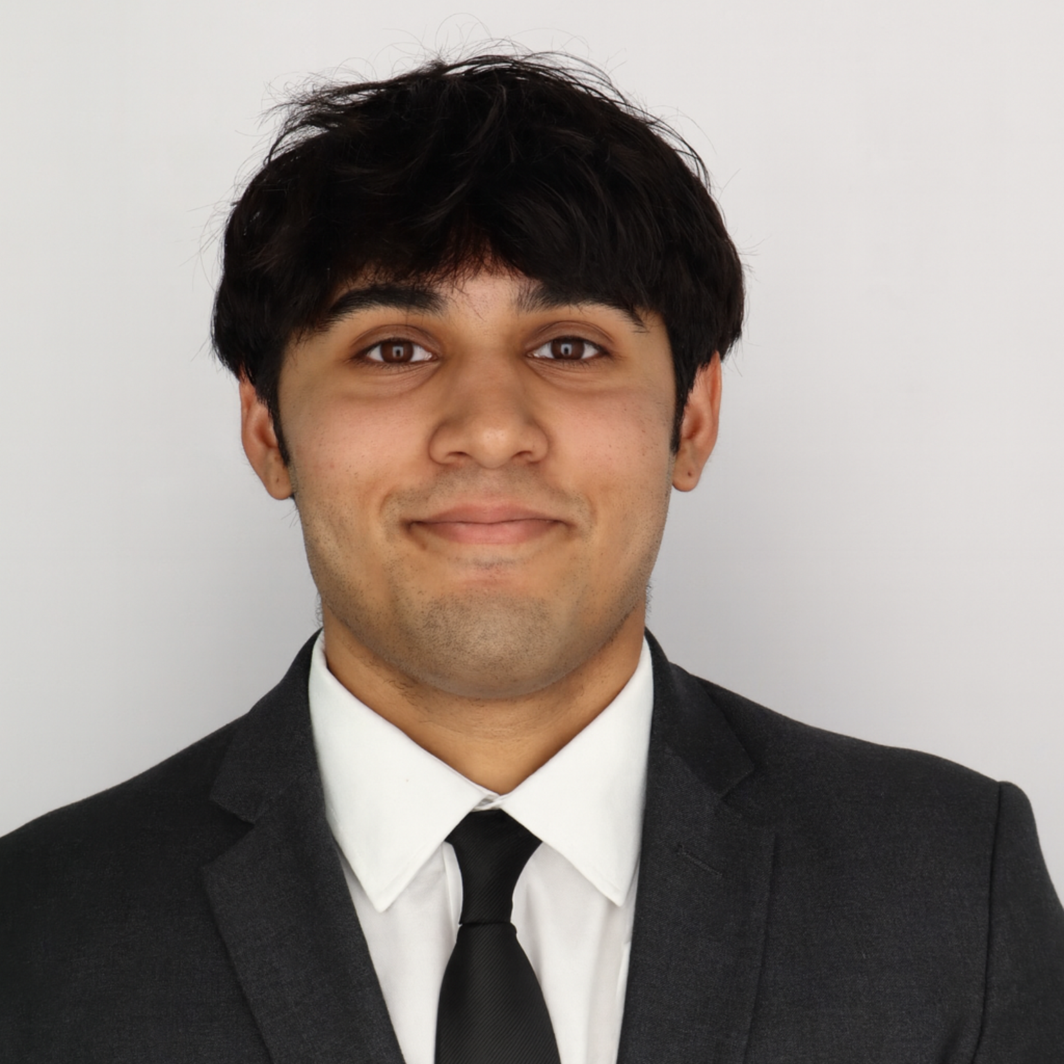 Person in a dark suit with a white shirt and black tie, smiling.