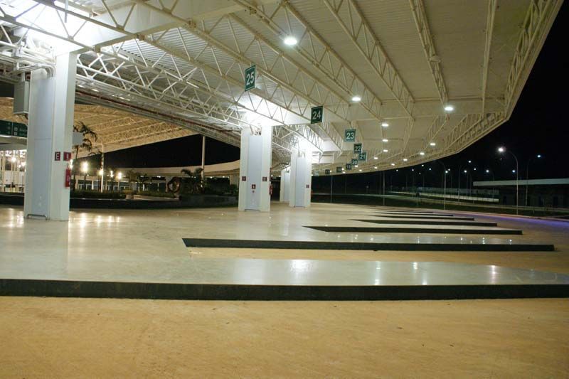 Estação rodoviária à noite; pilares brancos, longas fileiras de plataformas de ônibus sob um telhado curvo e iluminação.