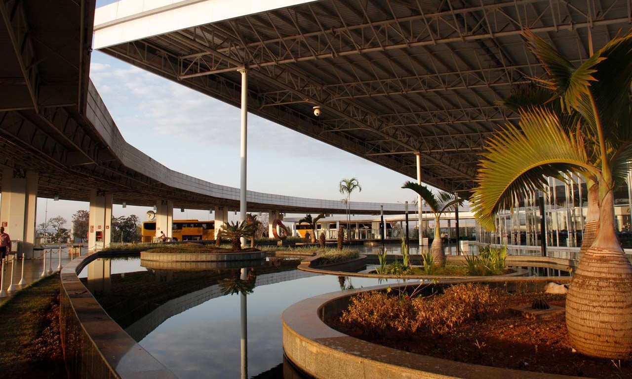 Passarela coberta com fonte e palmeiras.