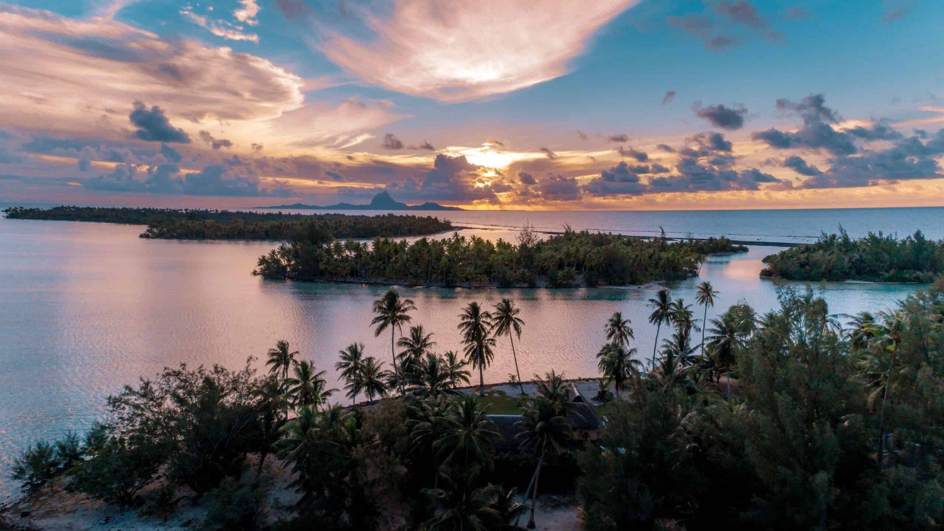 An aerial view of a tropical island in the middle of the ocean at sunset.