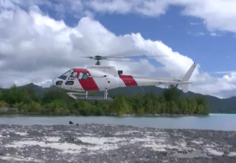 A red and white helicopter is flying over a body of water