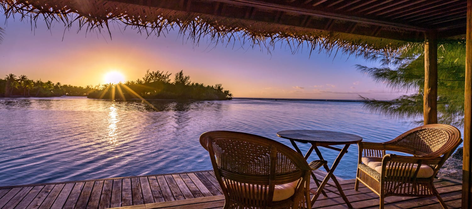A table and chairs on a dock overlooking a body of water at sunset.