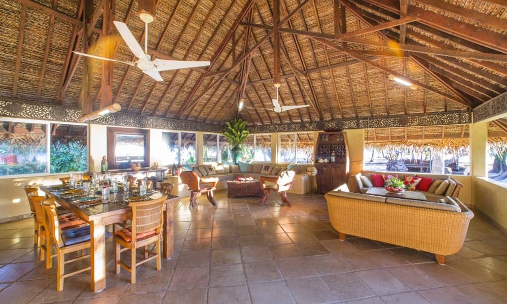 A large room with a thatched roof and a dining table and chairs.