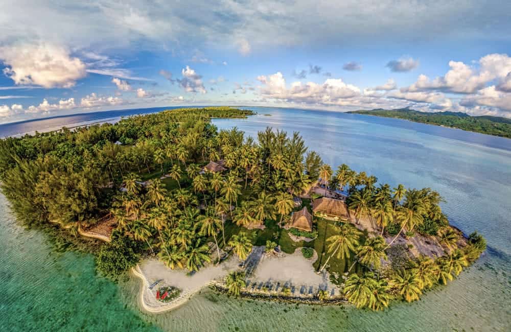 An aerial view of a small island in the middle of the ocean surrounded by palm trees.