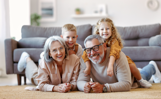 Two adults and two children lying on the floor in front of a sofa, smiling happily.