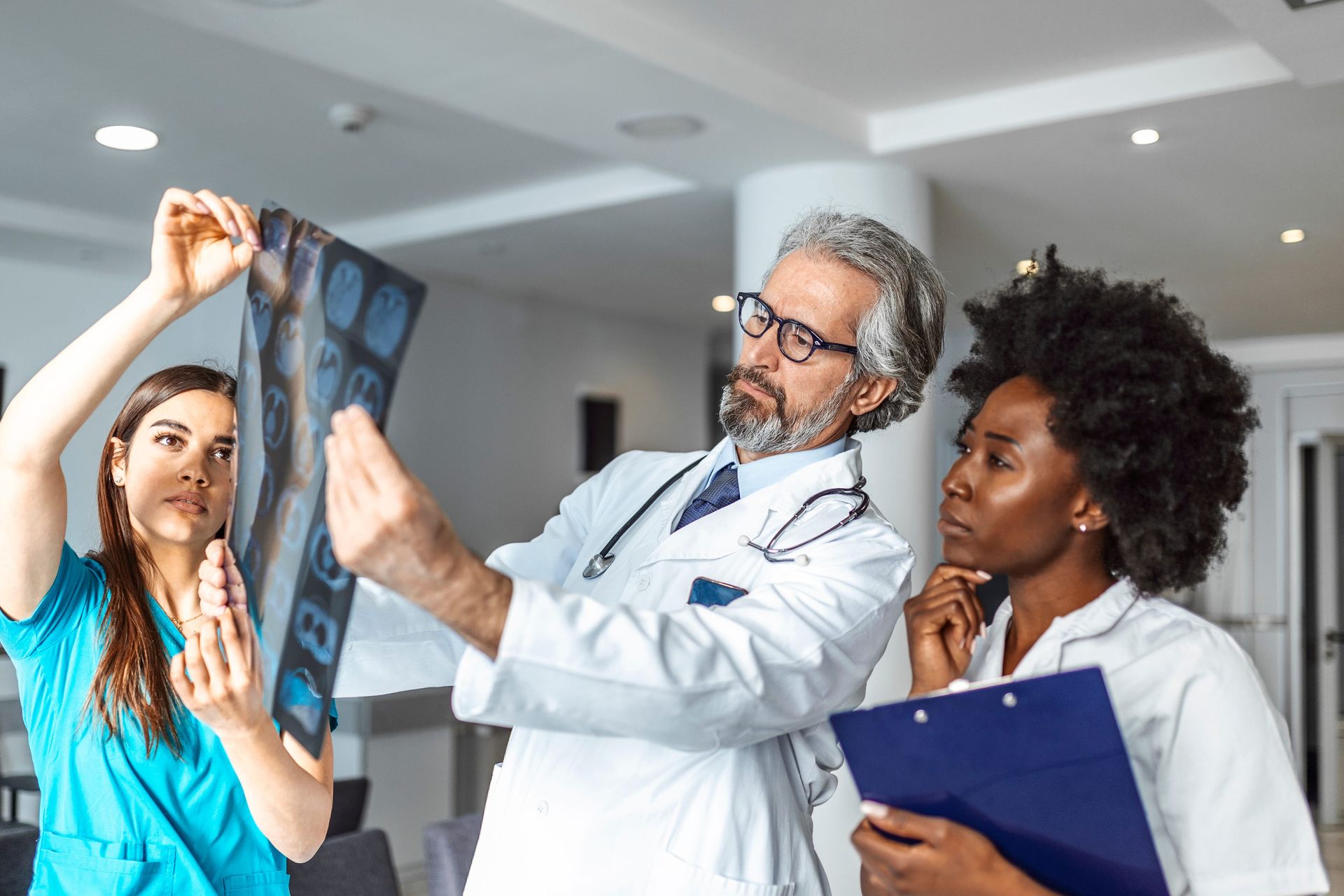 A doctor and two medical professionals examining an X-ray film in a brightly lit hospital setting.