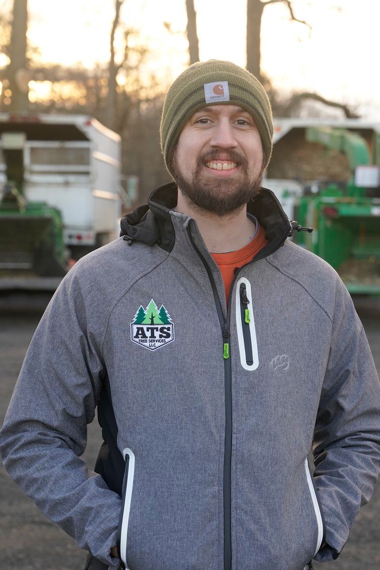 A man wearing a gray jacket and a green hat is standing in front of a truck.