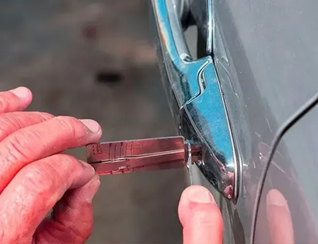 A person is using a tool to open a car door.