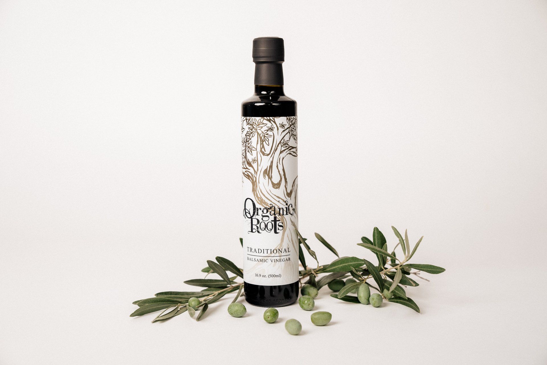 A bottle of olive oil is sitting next to a bunch of olives.