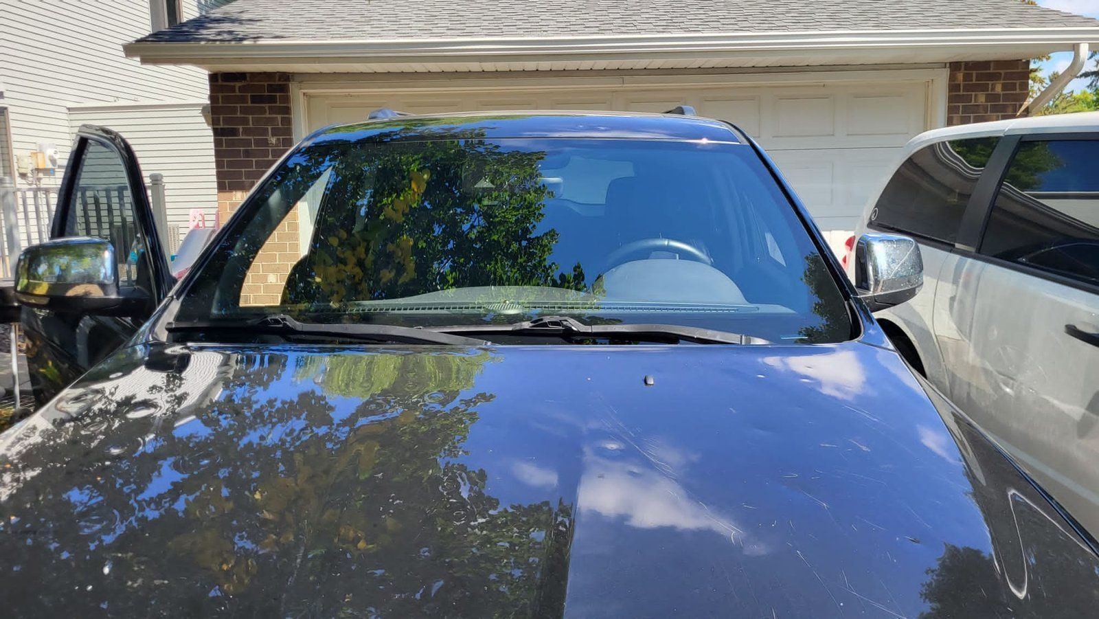 Black SUV with open door, parked in front of a house with a white garage door.