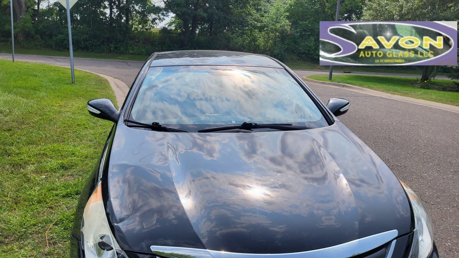 Black car with wet windshield parked near a sign for Savon Auto Service.