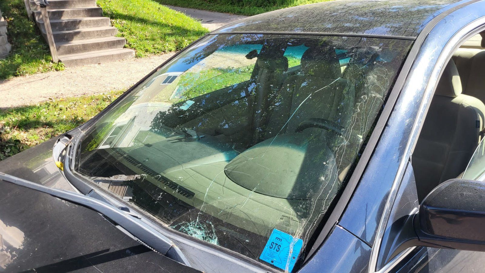 Car with cracked windshield, parked on a street. Blue tag on the bottom corner, stairs in background.