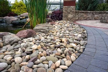 Curved garden path beside a bed of smooth river stones, with tall grasses and a stone wall