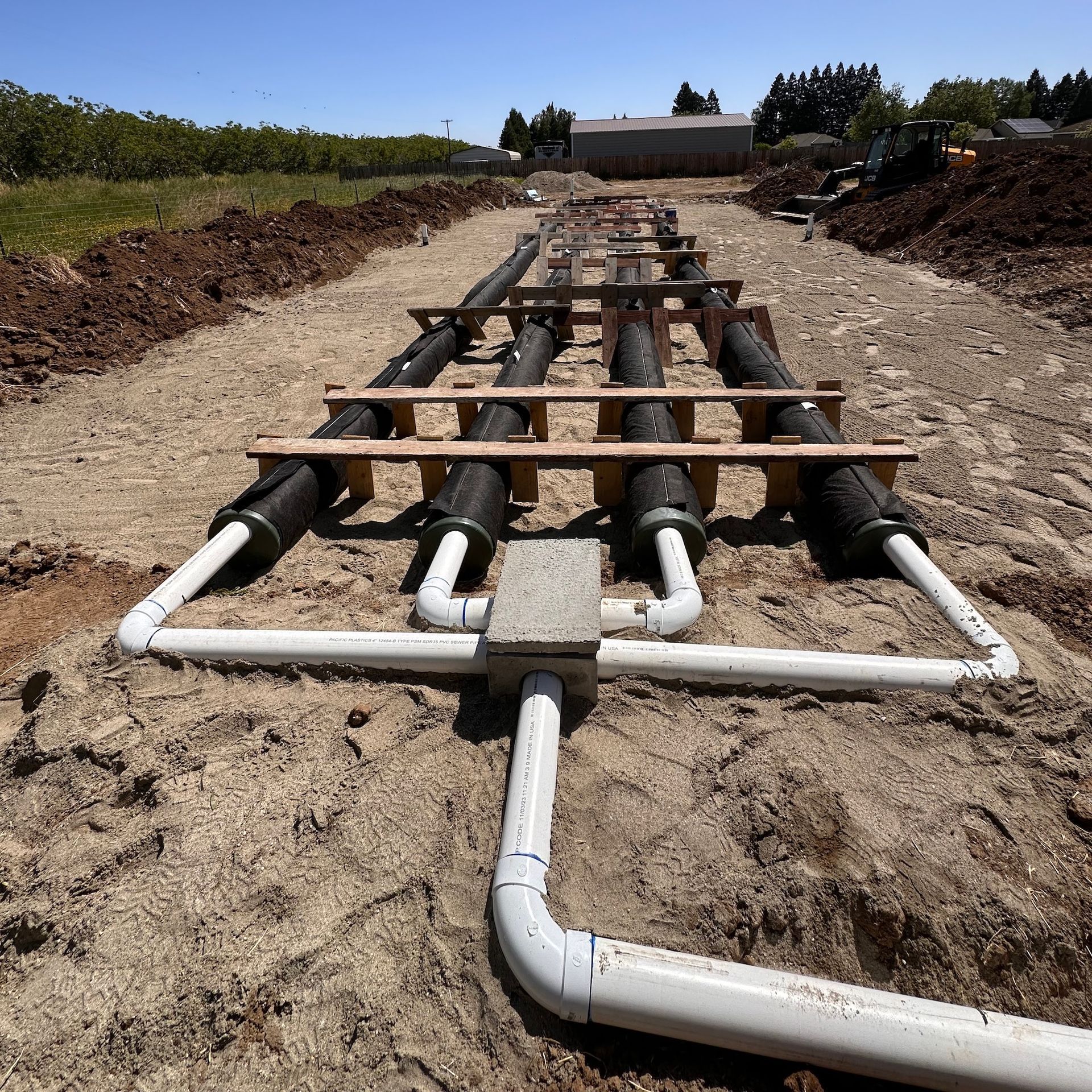 Pipes laid in trenches for construction, with supports and connections. Outdoor setting, bright daylight.