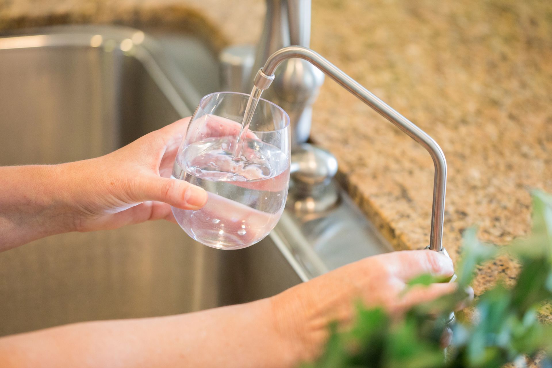 Hands fill a glass with water from a kitchen faucet.