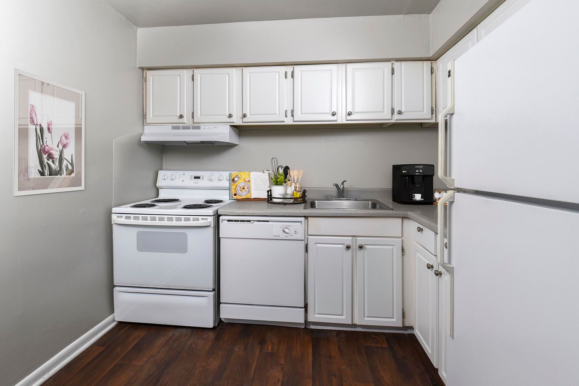 Compact apartment kitchen with white cabinets, stove, dishwasher, sink, and refrigerator at Chesapeake Pointe, offers apartments in Chesapeake, VA.