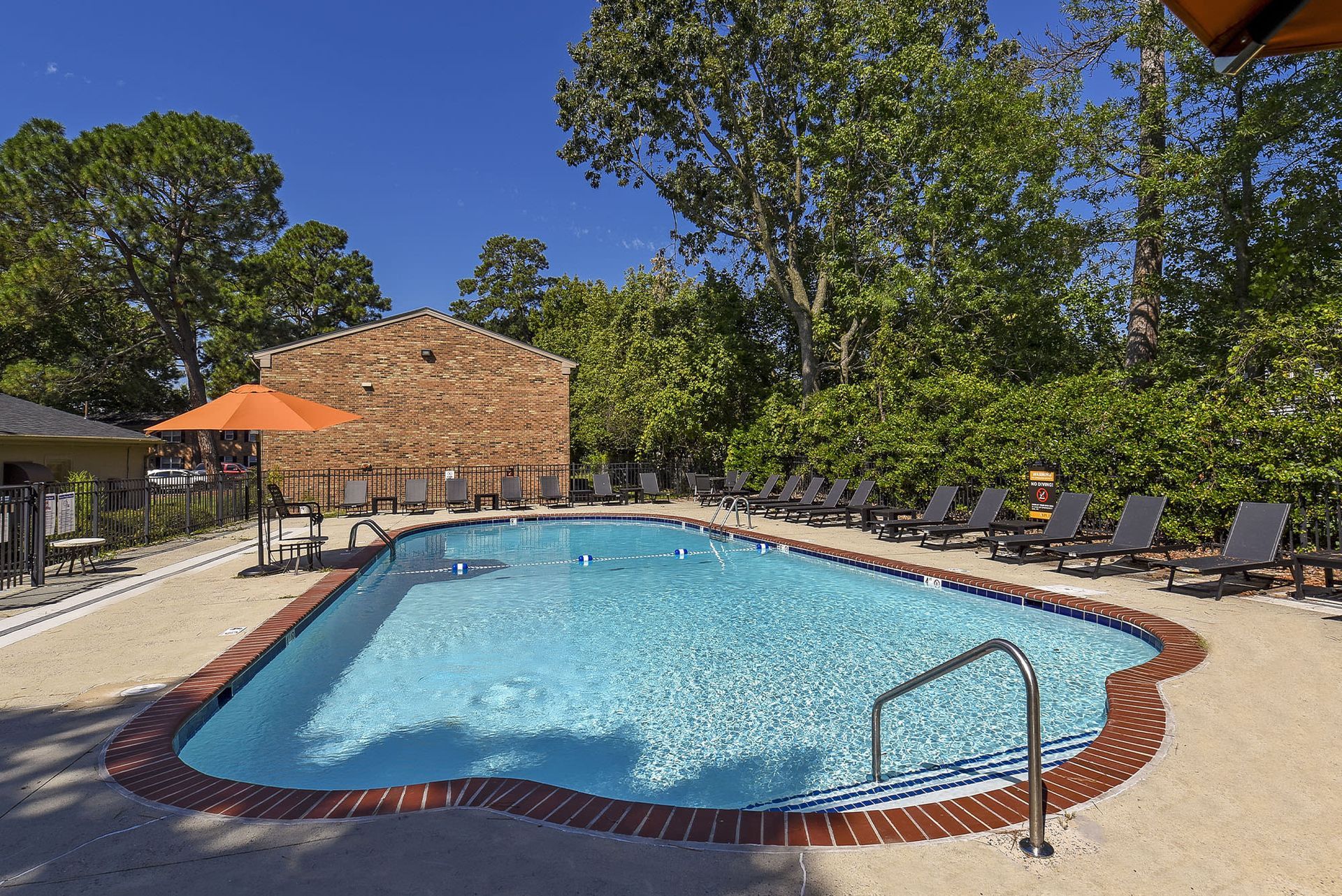 Outdoor community swimming pool with lounge chairs and an orange umbrella at Chesapeake Pointe, offers  pet-friendly apartments in Chesapeake, VA